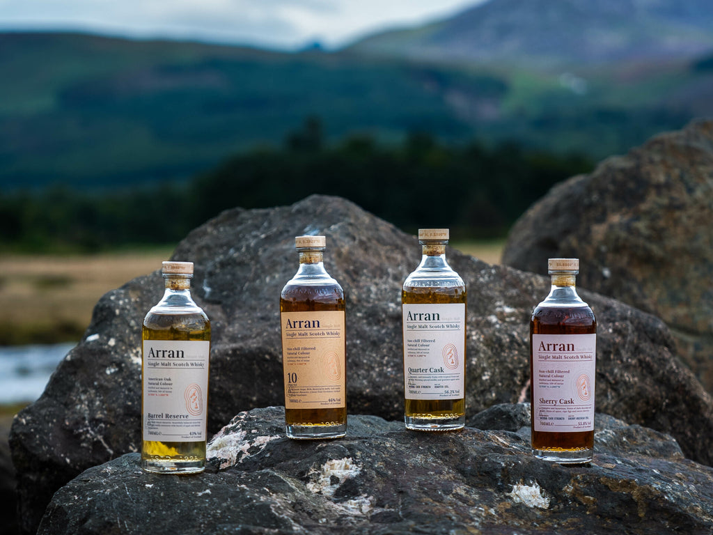 Four bottles of Arran whisky on rocks with a scenic background